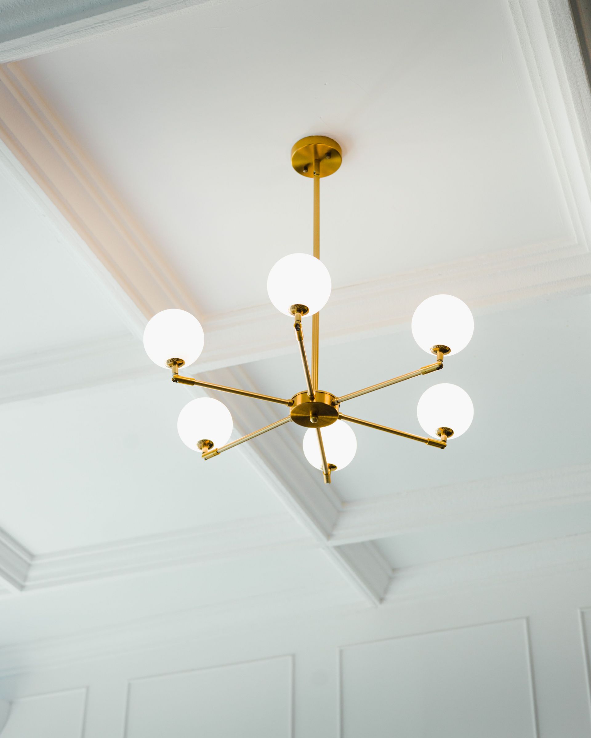 A stylish chandelier with a modern design hanging from a classic ceiling.