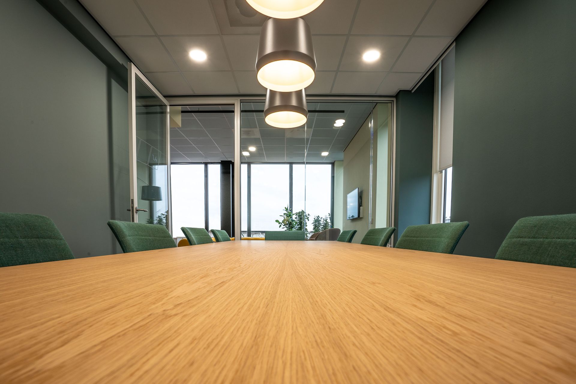 Spacious conference room with sleek wooden table, green chairs, and pendant lighting highlighting a minimalist style.