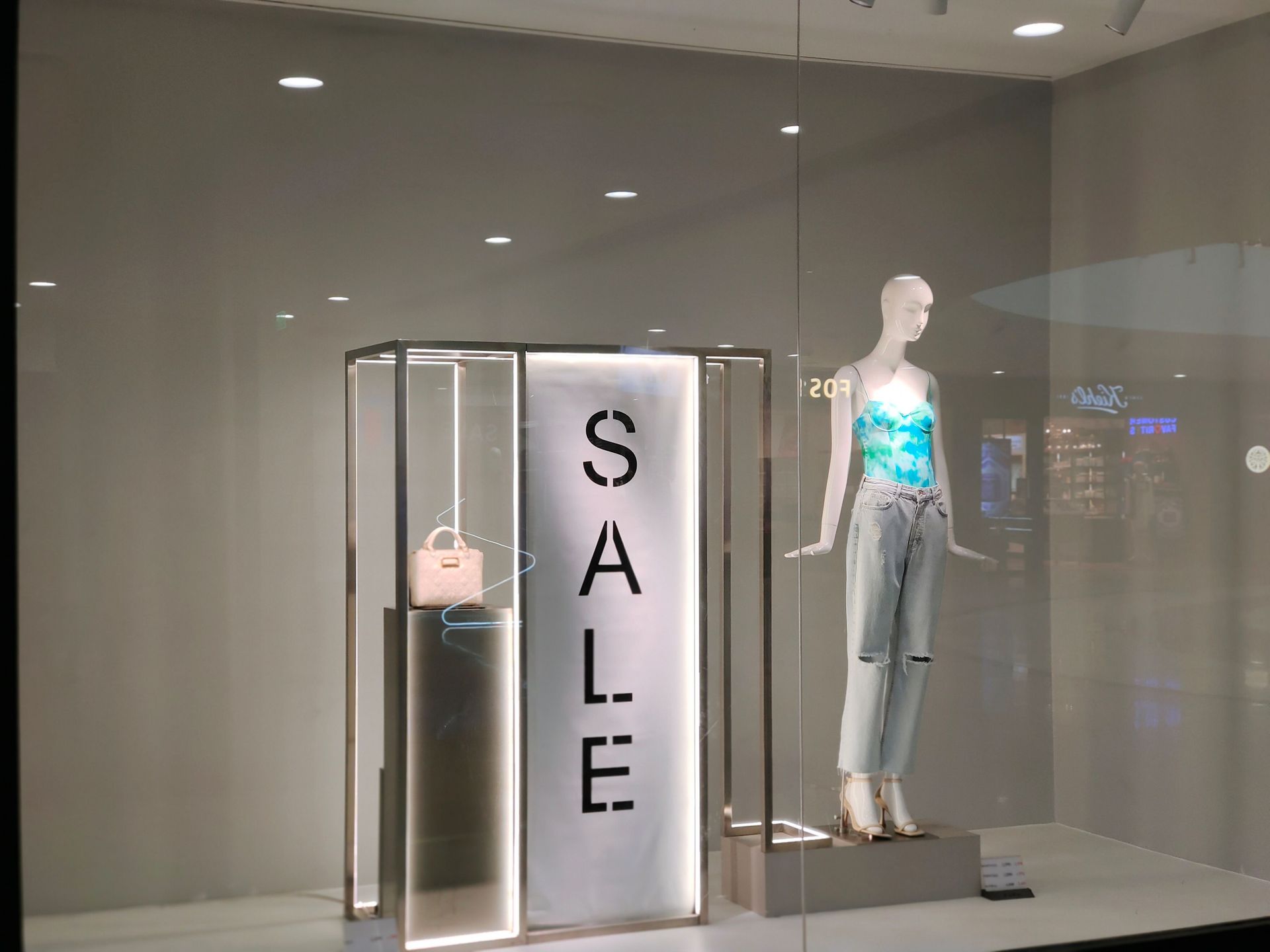 Stylish window display featuring sale sign and fashionable mannequin in trendy outfit.