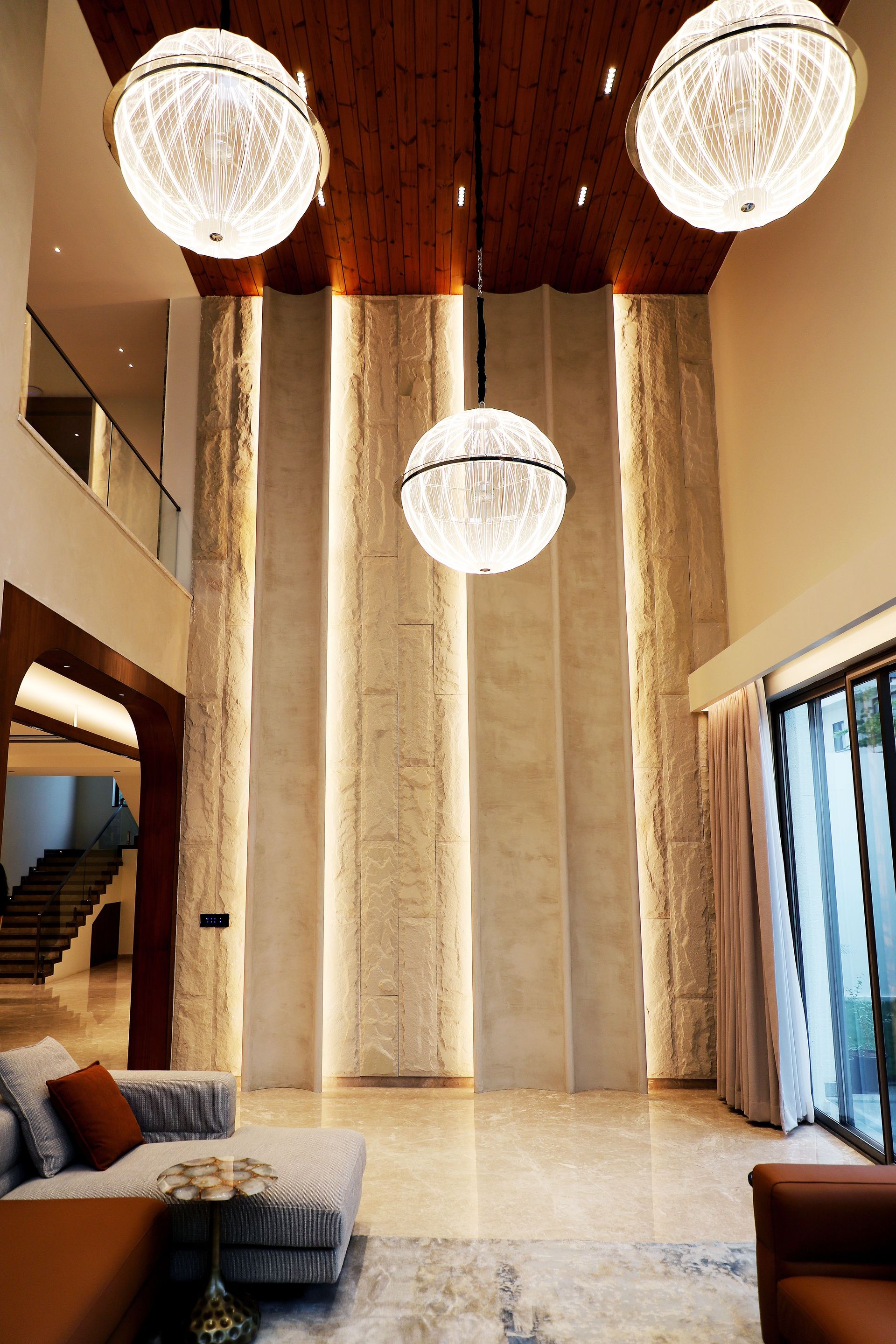 Spacious, modern living room featuring striking pendant chandeliers, elegant decor, and high ceilings.