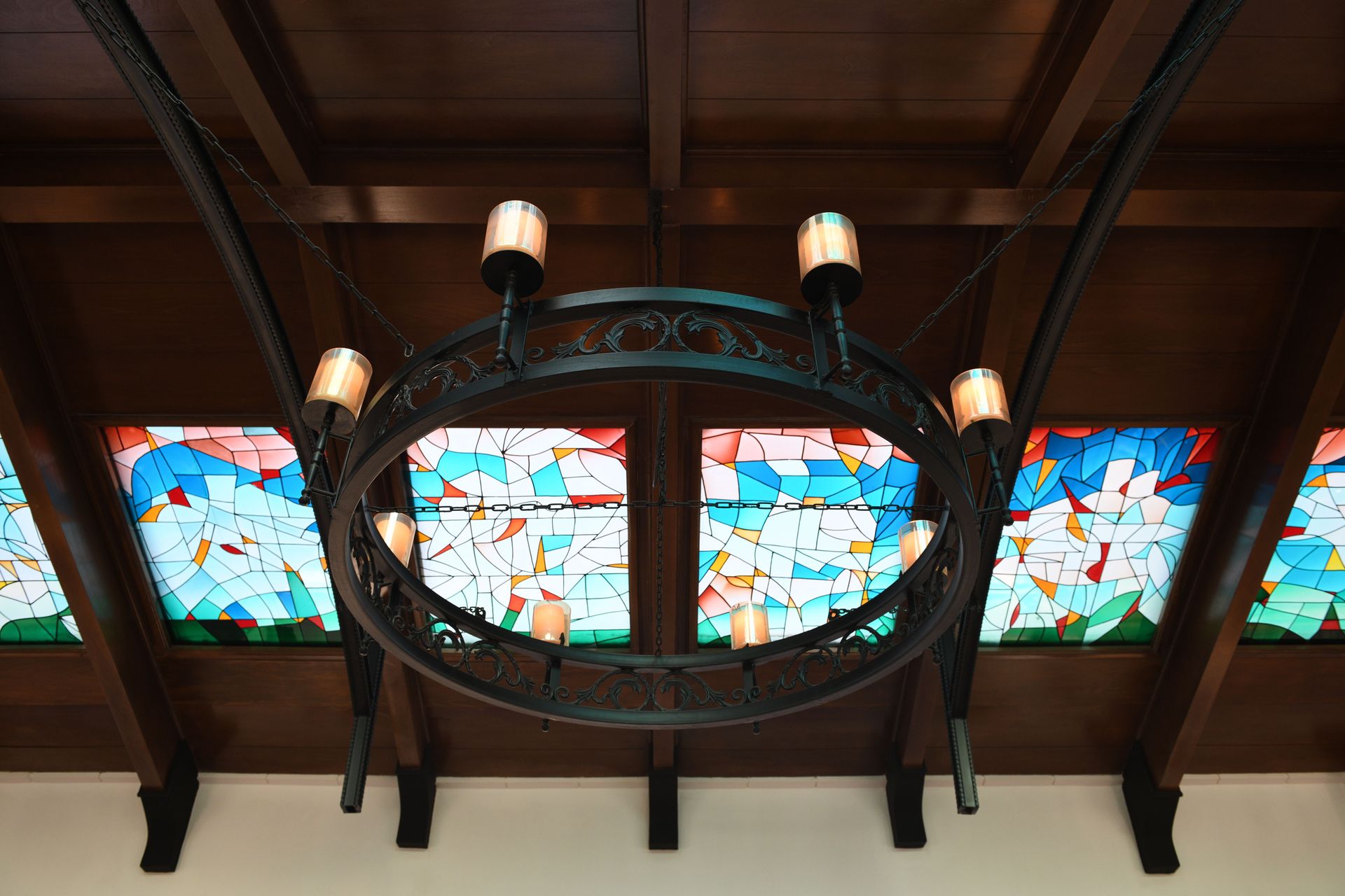 Ornate chandelier hanging beneath a vibrant stained glass ceiling, capturing warm ambiance.